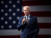 Joe Biden standing in front of an American flag, holding a microphone